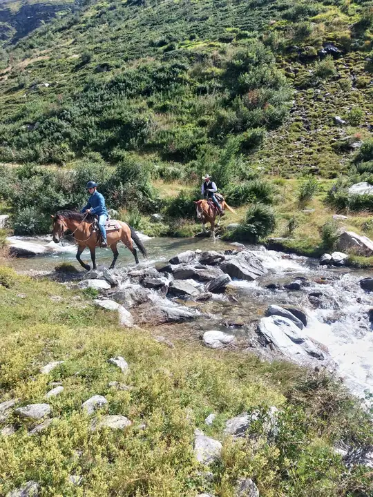 Due cavalieri guadano un torrente alpino